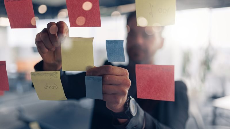 close up of businessman is glues sticky notes on motivation board in modern office